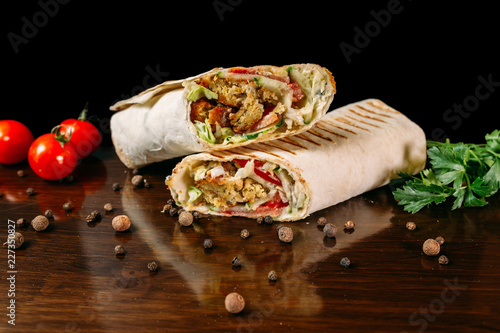 Shawarma sandwich gyro- fresh roll of thin lavash (pita bread) filled with grilled meat, mushrooms, cheese, cabbage, carrots, sauce, green. Traditional Eastern snack. On a wooden background