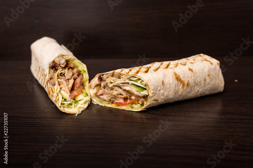 Shawarma sandwich - fresh roll of thin lavash (pita bread) filled with grilled meat, mushrooms, cheese, cabbage, carrots, sauce, green. Traditional Eastern snack. On a wooden background