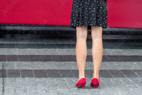 Woman wearing red shoes and polka dot dress waiting for the bus on the street