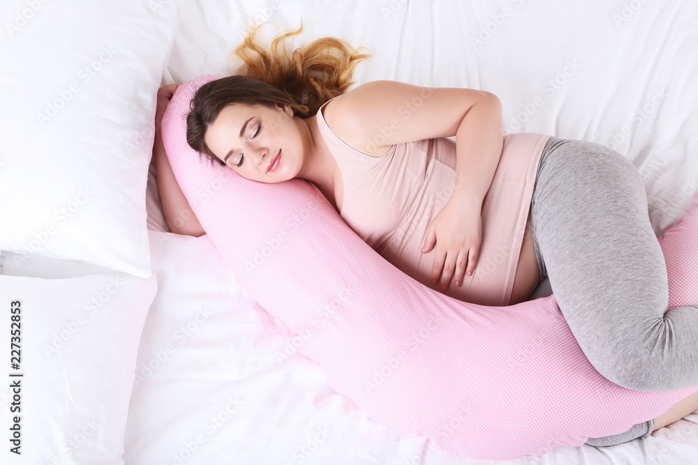 Young pregnant woman with pink pillow sleeping in bed - obrazy, fototapety, plakaty 