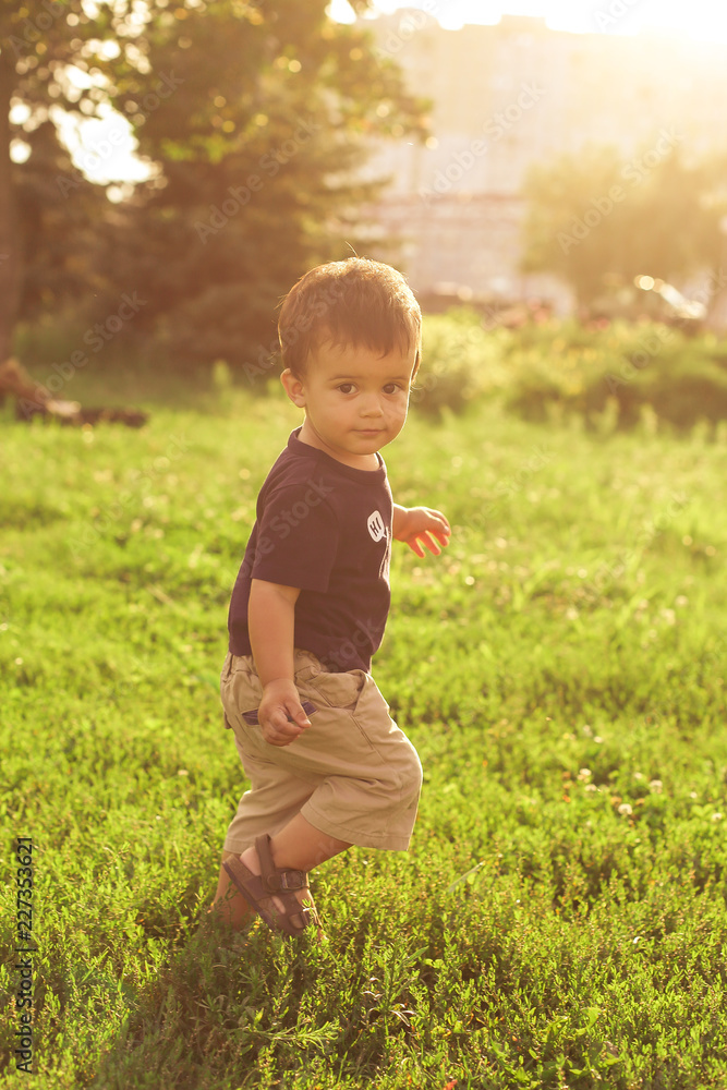 Sunny portrait of happy toddler in casual clothes, running in the park, green grass Sunny portrait of happy toddler in casual clothes, running in the park, green grass