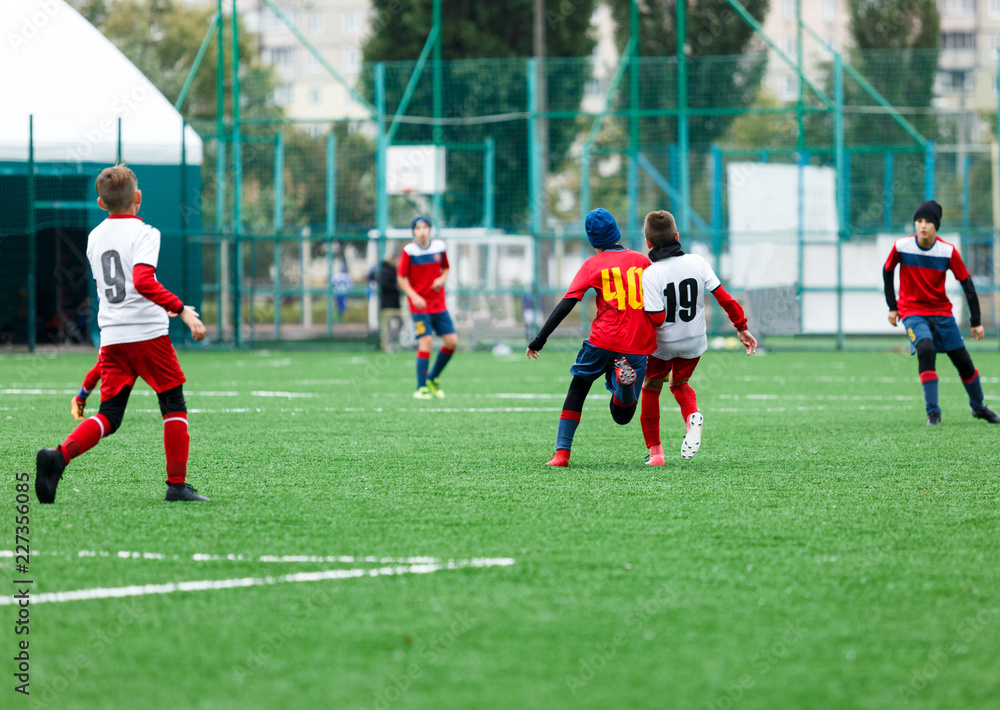 Obraz premium football teams - boys in red, blue, white uniform play soccer on the green field. boys dribbling. dribbling skills. Team game, training, active lifestyle, hobby, sport for kids concept