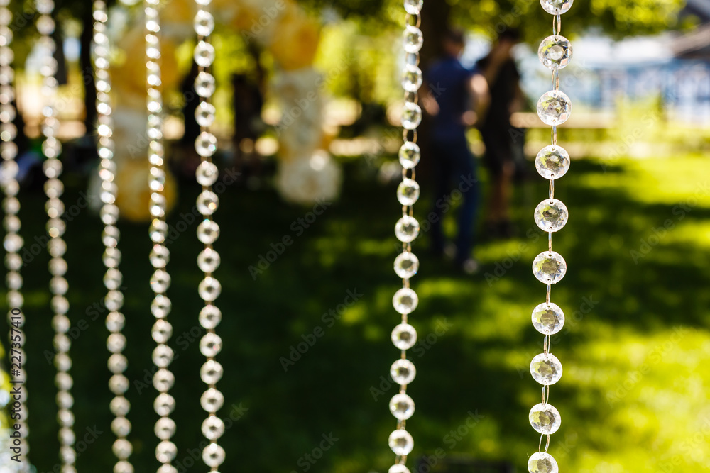 Fragment of creatively decorated wedding arch with hanging glass beads on green background Fragment of creatively decorated wedding arch with hanging glass beads on green background