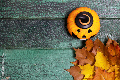 Top view image of autumn leaves over wooden textured background with halloween pumpkin