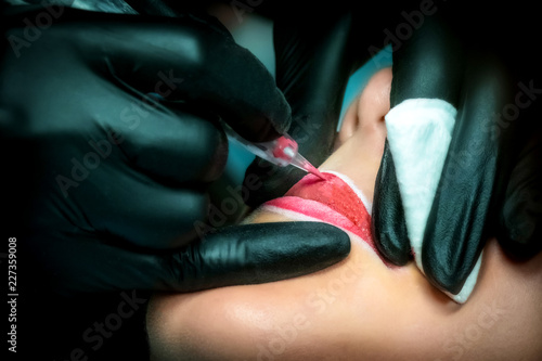Hands in black gloves apply permanent makeup on the lips. Woman s face with painted lips. Permanent makeup. Beauty salon. Cosmetic procedures. Red lipstick.