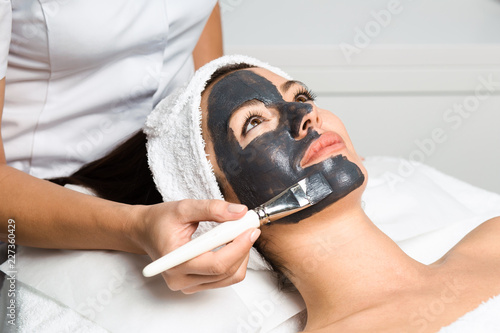 Beautiful woman receiving clay facial mask with rejuvenating effects in spa beauty salon.