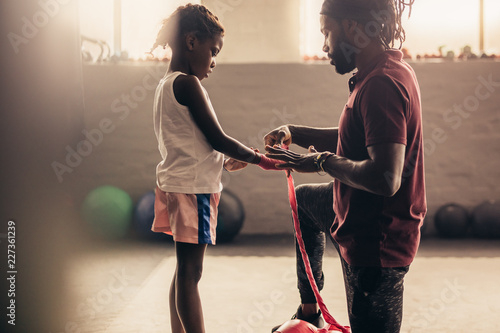 Fényképezés Boxing trainer wrapping hands of a kid with bandage