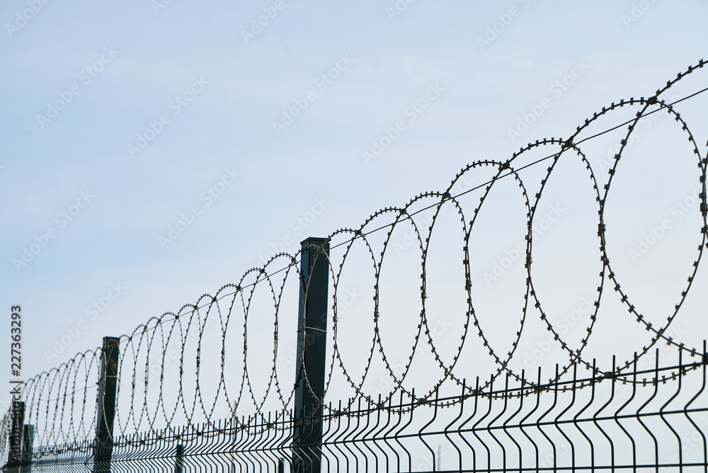 Barbed wire against cloudy sky, close-up. Metal fence with barbed wire, outdoors Barbed wire against cloudy sky, close-up. Metal fence with barbed wire, outdoors