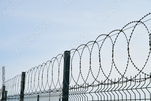 Barbed wire against cloudy sky, close-up. Metal fence with barbed wire, outdoors 