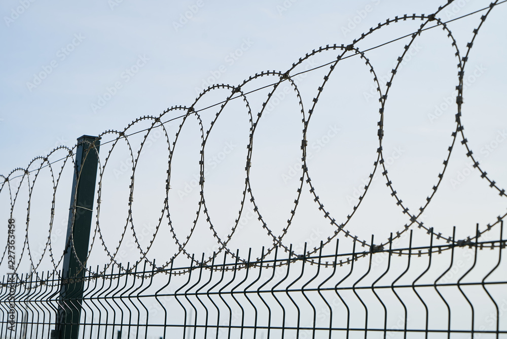Barbed wire against cloudy sky, close-up. Metal fence with barbed wire, outdoors Barbed wire against cloudy sky, close-up. Metal fence with barbed wire, outdoors