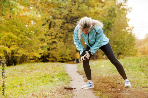 the athlete has a sore knee while jogging, and he stands in pain and massages his sore knee in a park in the fall