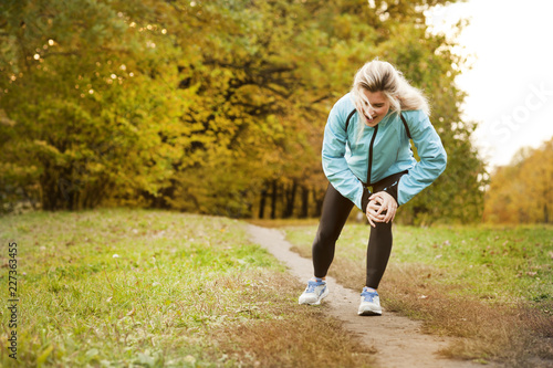 the athlete has a sore knee while jogging, and he stands in pain and massages his sore knee in a park in the fall