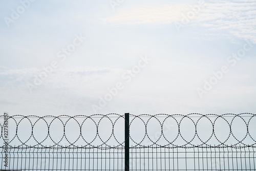Barbed wire against cloudy sky, close-up. Metal fence with barbed wire, outdoors  © Gecko Studio