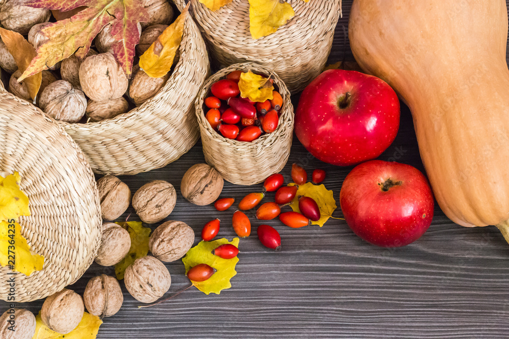 Walnuts, red apples, rose hips, pumpkin and yellow leaves on a wooden surface, healthy food from nature. Concept of autumn background