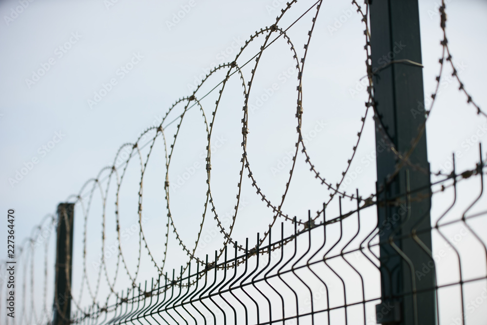 Barbed wire against cloudy sky, close-up. Metal fence with barbed wire, outdoors Barbed wire against cloudy sky, close-up. Metal fence with barbed wire, outdoors