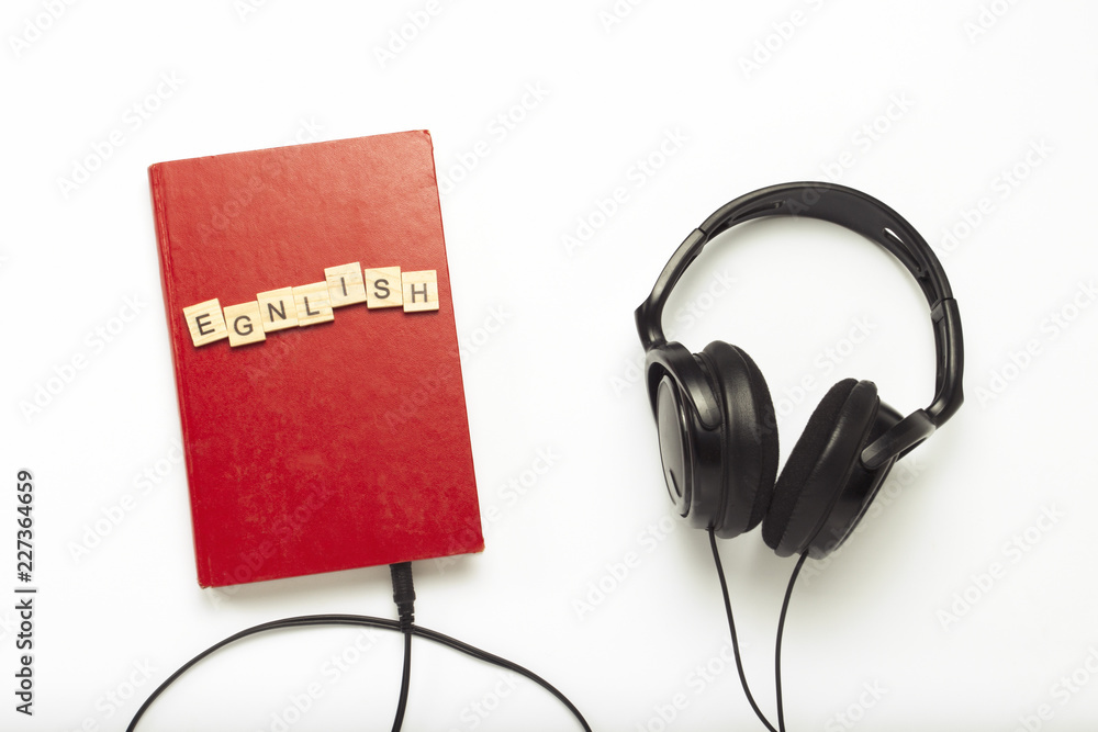 Book with a red cover with text English and black headphones on a white background. Concept of audiobooks, self-education and learning English independently. Flat lay, top view Book with a red cover with text English and black headphones on a white background. Concept of audiobooks, self-education and learning English independently. Flat lay, top view