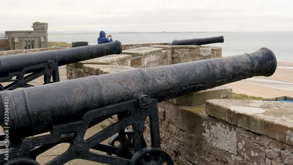 An unidentifiable tourist takes cell phone photo of Bamburgh Beach and the North Sea from the Bamburgh Castle with canons fortifying the castle aimed out to sea-Northumberland, England An unidentifiable tourist takes cell phone photo of Bamburgh Beach and the North Sea from the Bamburgh Castle with canons fortifying the castle aimed out to sea-Northumberland, England