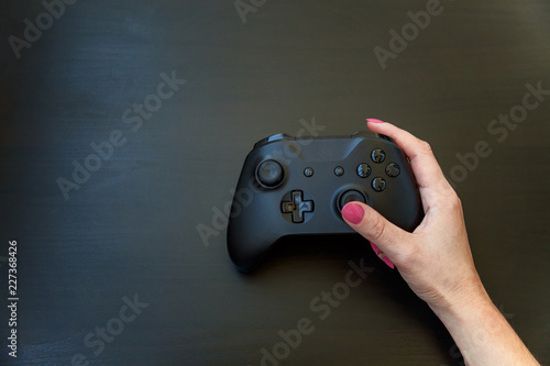 Woman hand holding black joystick gamepad, game console on black background. Computer gaming competition videogame control confrontation concept