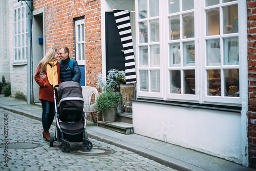 Happy young parents with baby stroller in the street of Lubeck (Germany)