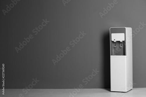 Modern water cooler against gray wall with space for text