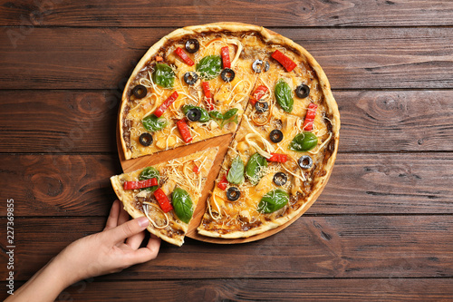 Woman holding delicious homemade pizza slice on wooden background