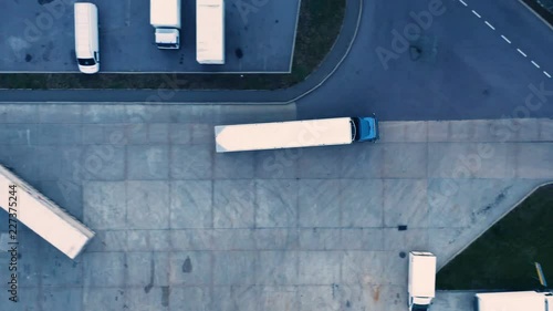 Aerial top view of a of semi-trailer truck traveling through the parking lot of the warehouse/ storage building/ loading area photo