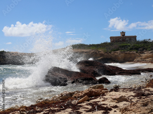 Waves crash into rock; lighthouse in background photo