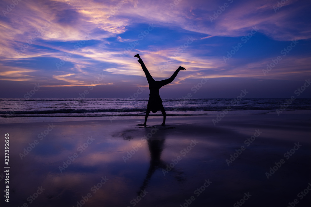Man does handstand on beach at sunset