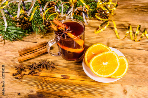 Cup of mulled wine with cinnamon, christmas decorations, sliced orange and fir tree branches on wooden table