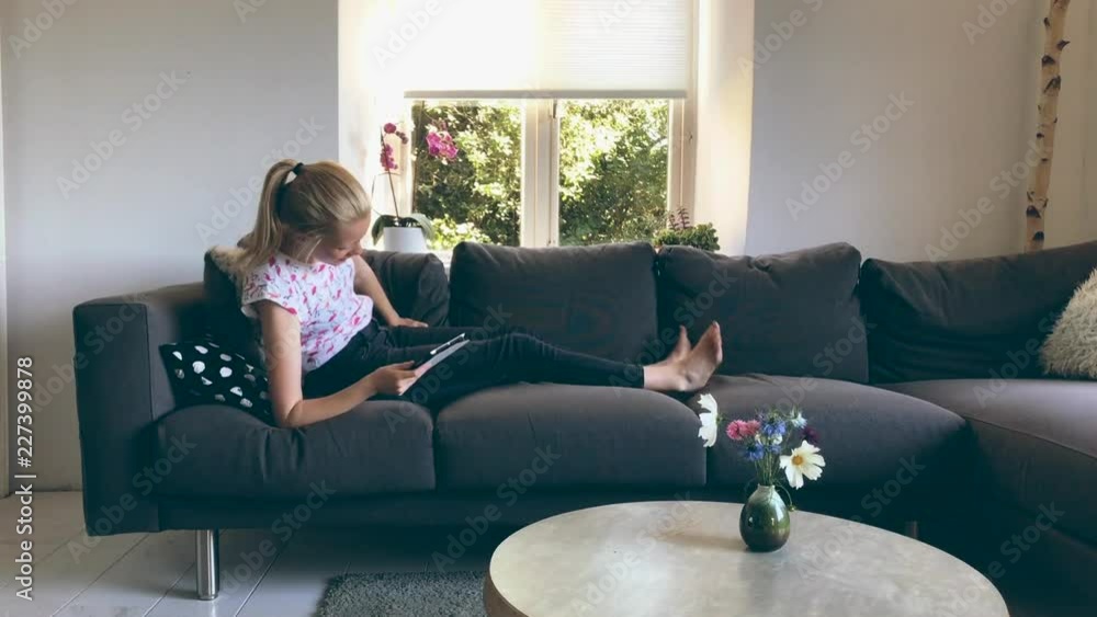 Young woman sitting on a couch with a tablet on her lap connected to ...