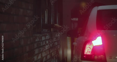 Drive-thru cashier accepts money from customer for their order at a fast food restaurant in the city during the night time.