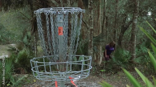 Disc golf basket in foreground. Disc golfer in the background missing a putt to the basket photo