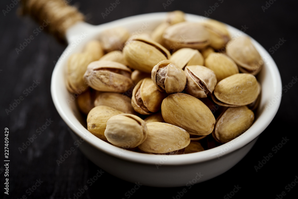 Obraz premium white bowl full of delicious pistachios on an old black table in a pub