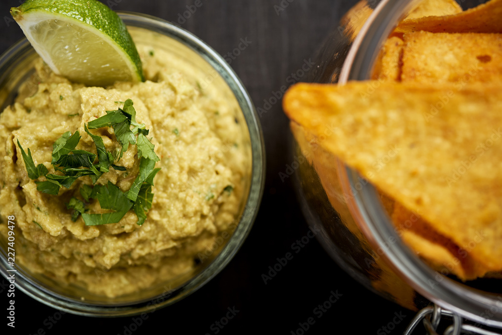 bowl of fresh delicious guacamole and a jar of nachos on an old black wooden table in a pub bowl of fresh delicious guacamole and a jar of nachos on an old black wooden table in a pub