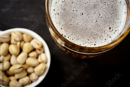 view of the foam of delicious beer in a glass and pistachios in a white bowl