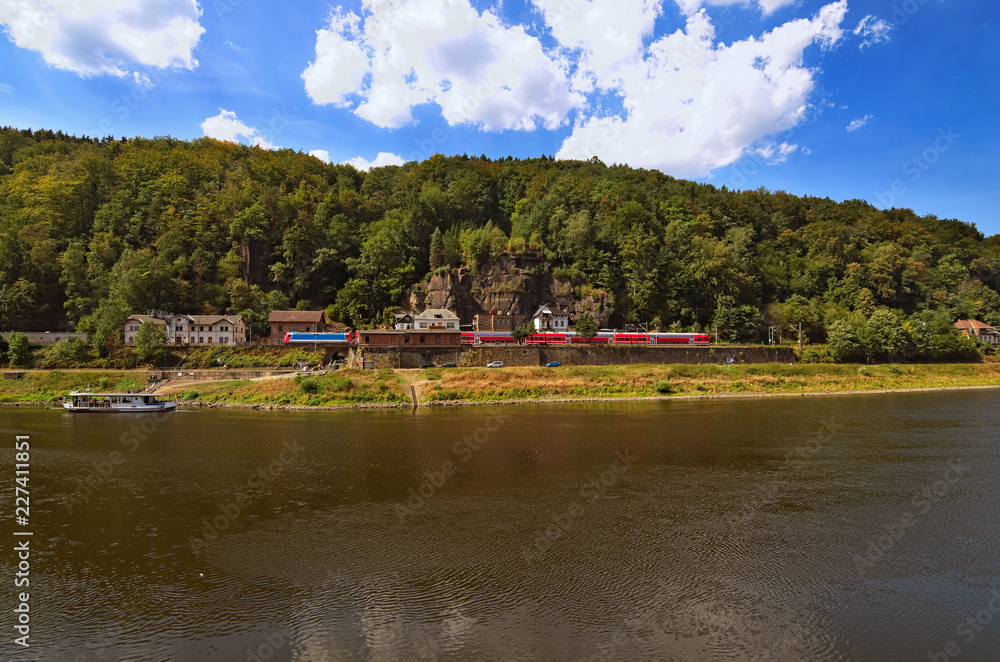 Red train at the Railway station on picturesque bank of the Elbe River of the Elbe river. Small white ferryboat connects the Czech Republic and Germany. Hrensko, Cech Republic