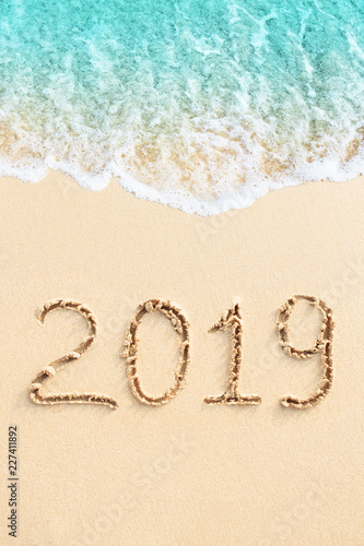 New Year 2019 handwritten on the sandy beach with blue ocean wave