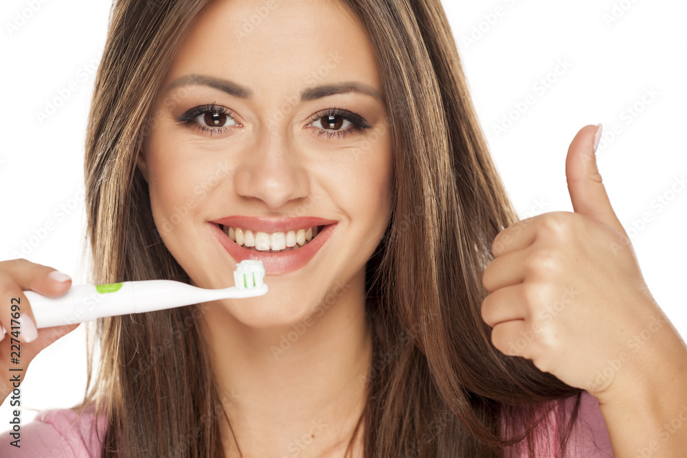 young woman holding electric tooth brush on white background and showing thumbs up young woman holding electric tooth brush on white background and showing thumbs up