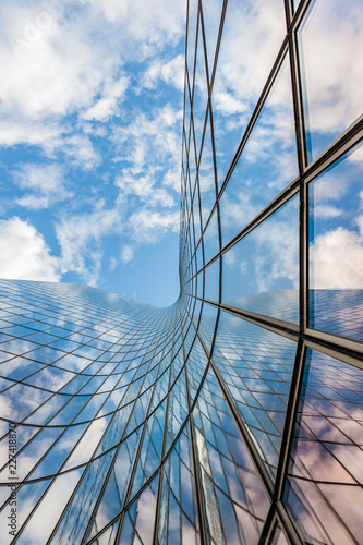 Glass curved building reflecting blue sky and white clouds low angle view