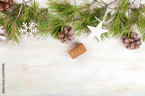 Christmas background with fir tree branches, cones, snow, xmas decorations and a champagne cork with a place for text, top shot