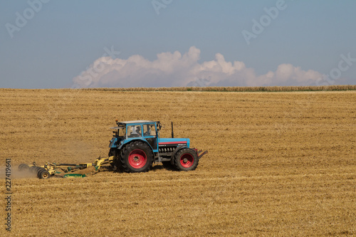 Traktor auf einem gem  hten Feld im Sonnenschein