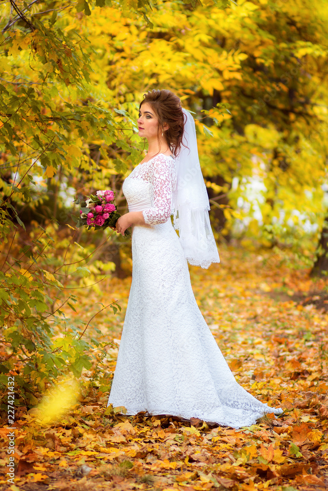 The bride in a wedding dress walks in the autumn park