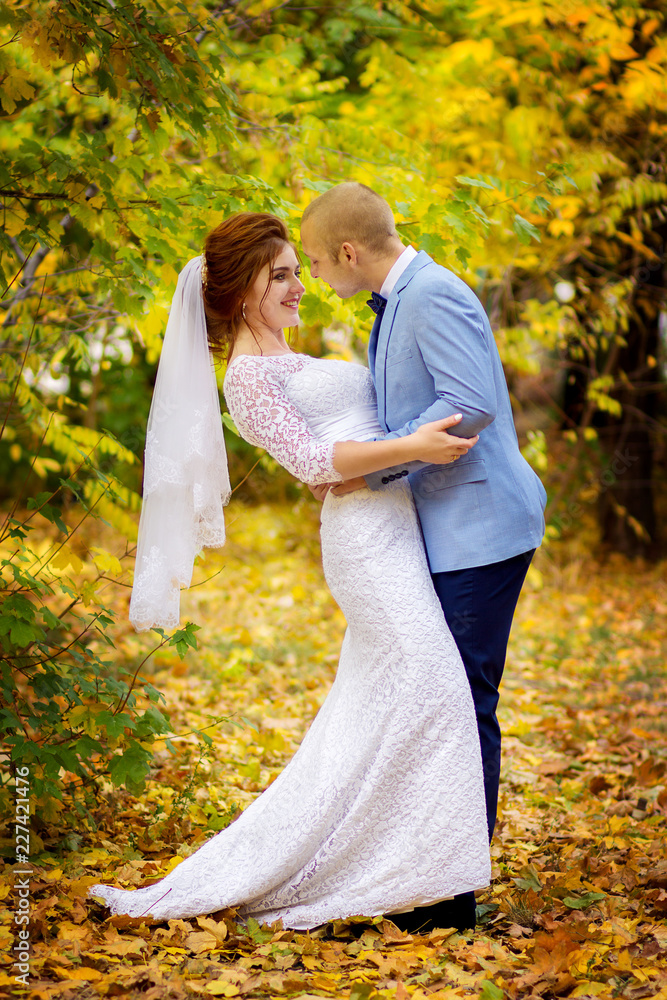 The groom kiss the bride in the autumn park. Happy newlyweds pose at a yellow tree The groom kiss the bride in the autumn park. Happy newlyweds pose at a yellow tree