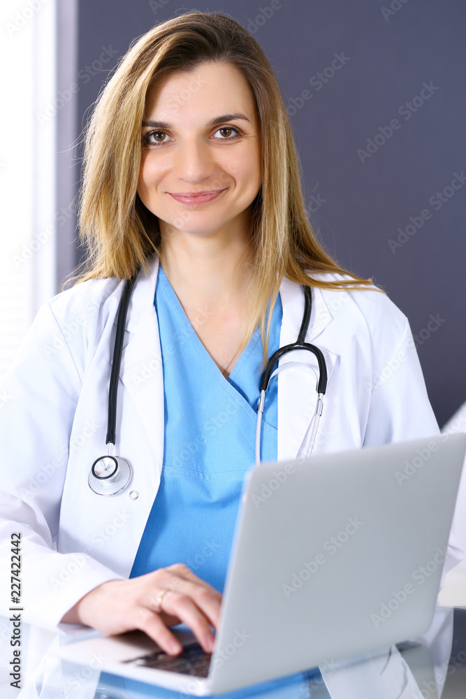 Woman doctor at work using laptop computer in hospital office. Portrait of female physician. Medicine and health care concept Woman doctor at work using laptop computer in hospital office. Portrait of female physician. Medicine and health care concept
