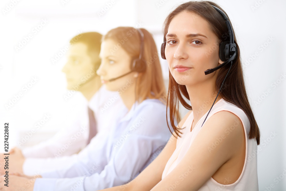 Naklejka premium Call center operators. Focus on young cheerful smiling woman in headset. Business and customer service concepts