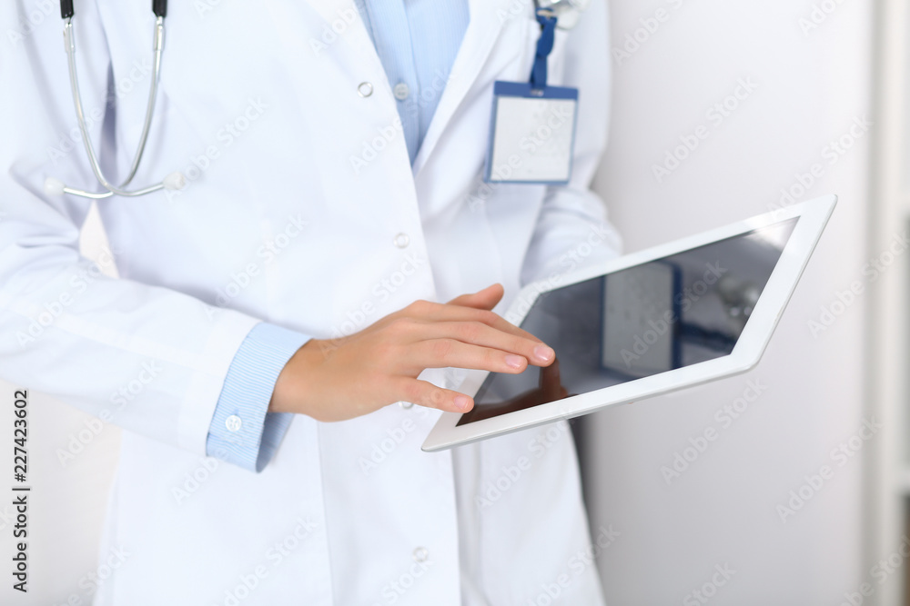 Doctor woman using tablet in clinic office. Unknown female physician at work while standing straight at hospital, close-up. Medicine and healthcare concept Doctor woman using tablet in clinic office. Unknown female physician at work while standing straight at hospital, close-up. Medicine and healthcare concept