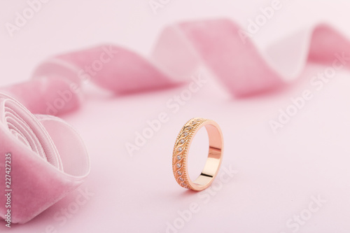 Pink gold wedding ring with diamonds and wave pattern on pink background