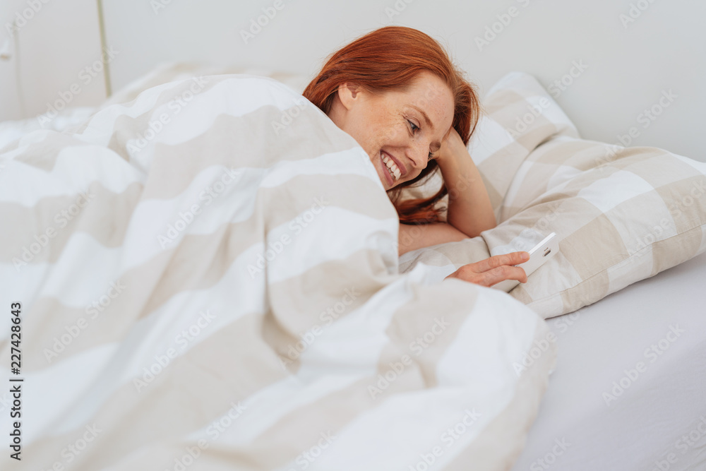 Smiling young woman in bed with smartphone Smiling young woman in bed with smartphone