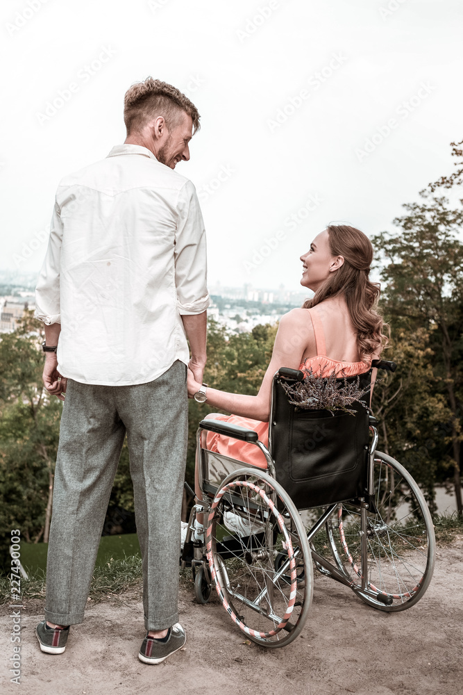 Lovely date. Peaceful disabled young girl sitting in the wheelchair and enjoying spending time with her boyfriend Lovely date. Peaceful disabled young girl sitting in the wheelchair and enjoying spending time with her boyfriend
