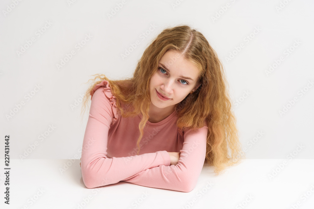 Studio portrait of a beautiful girl blonde teenager on a white background sitting at the table. Studio portrait of a beautiful girl blonde teenager on a white background sitting at the table.